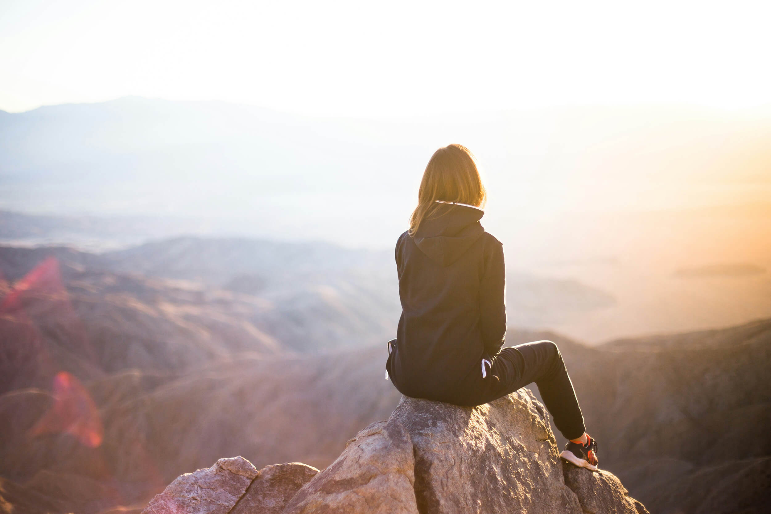Woman perched on a rock at the top of a mountain